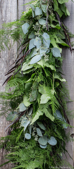 Designers Choice Fresh Extra Full Four Item Garland with Plumosa, Agonis, Salal and Seeded Eucalyptus Hanging on Wood Fence